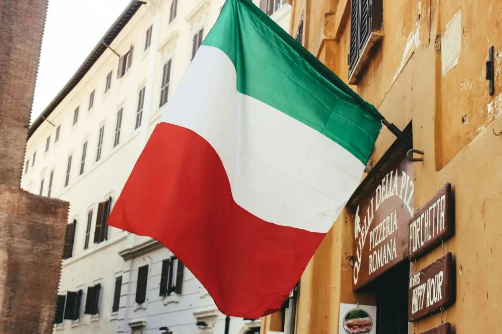 An Italian flag waves in front of a building; Italian citizenship applications reform legislation will take effect in 2025 if passed in Italy’s Senate, with huge implications for Italian diaspora communities.